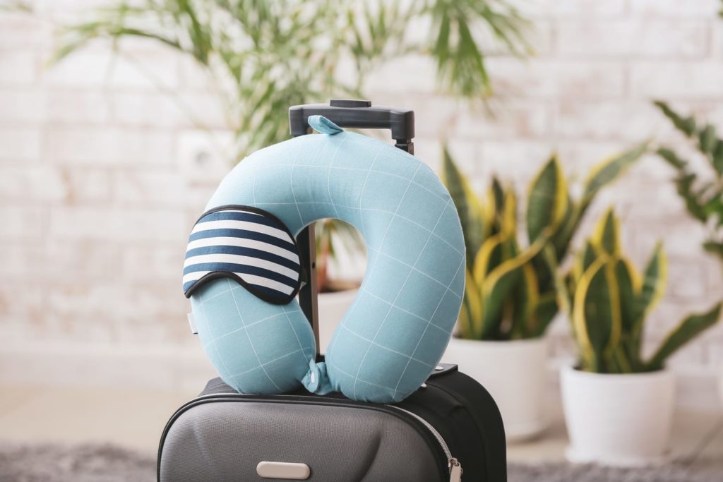 Travesseiro de viagem em cima de mala com máscara de dormir