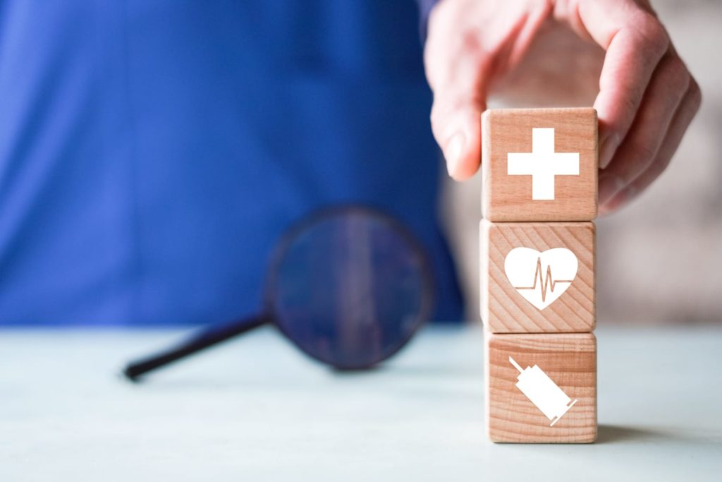 Pessoa com roupa de enfermeiro empilhando blocos de madeira com símbolos médicos